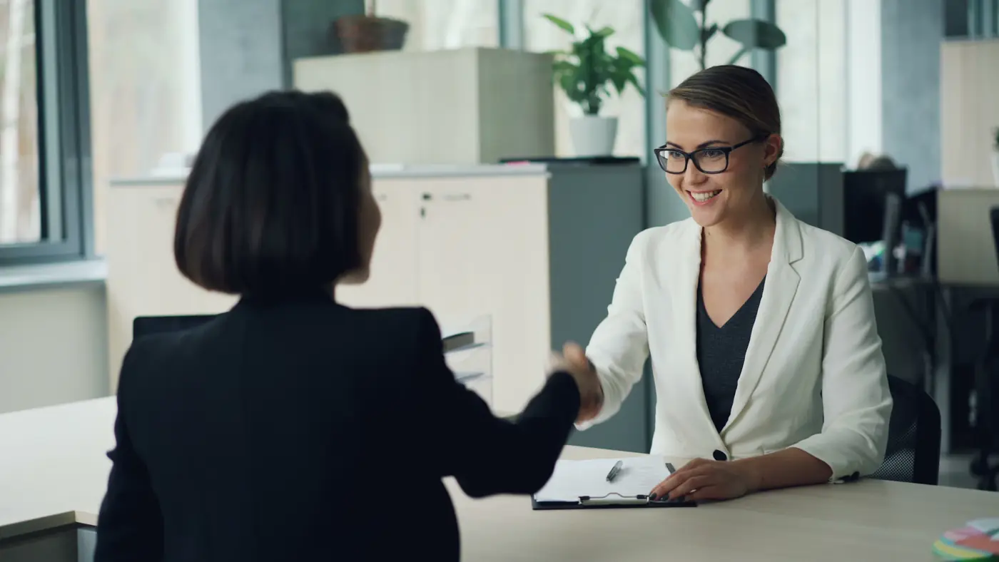 Een consultant in een licht kantoor geeft een kandidaat een hand aan het begin van een gesprek