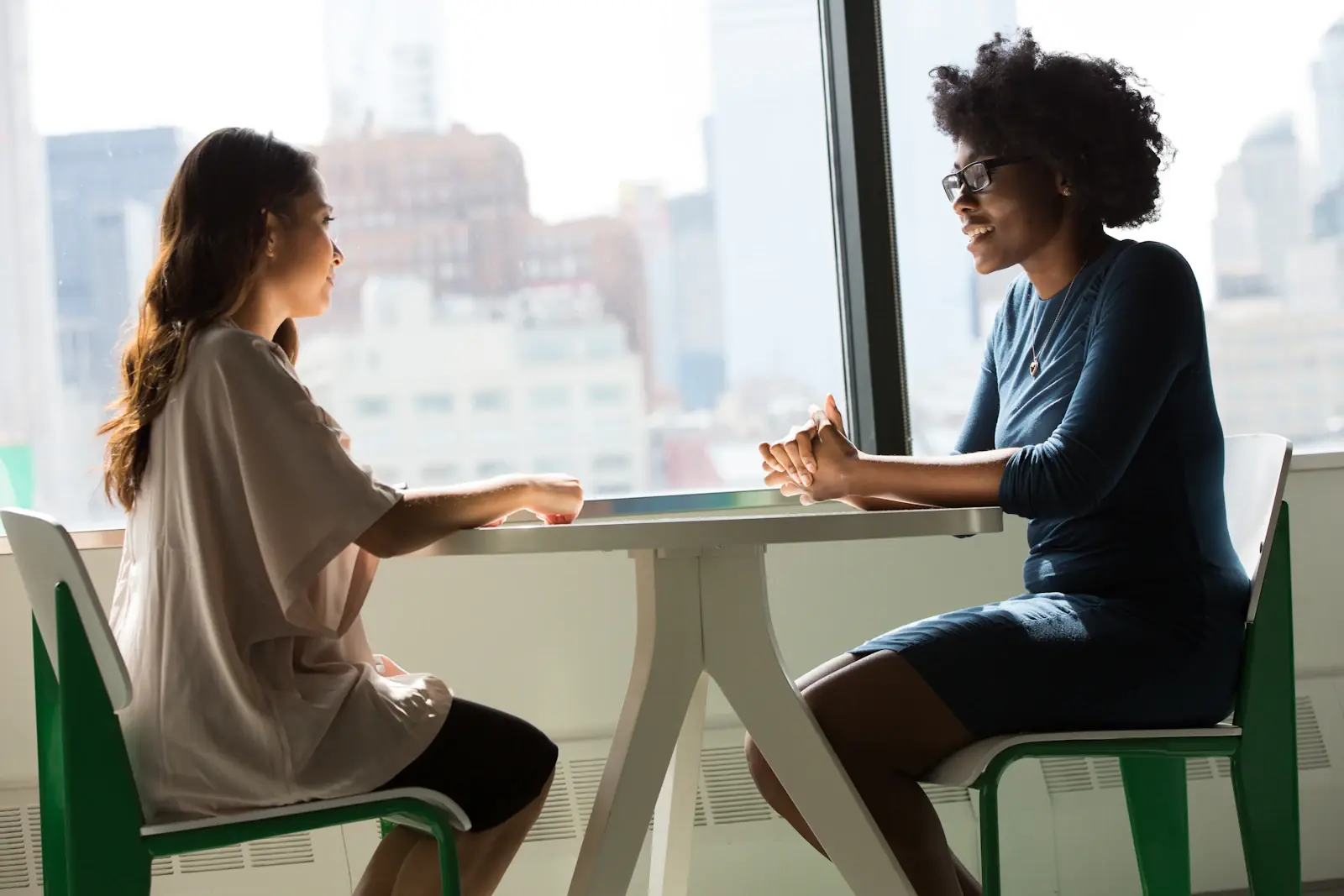 Twee vrouwen in gesprek aan een tafel bij een groot raam