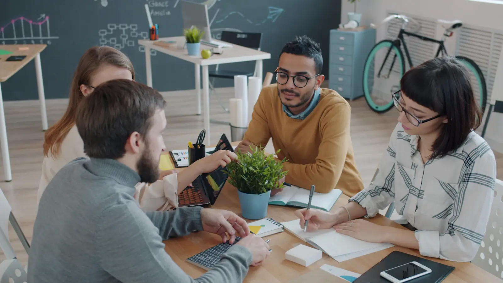 Een team overlegt rond een tafel met notitieblokken en laptops in een kantoor